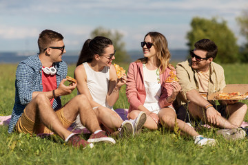 friendship, leisure and food concept - group of smiling friends eating pizza at picnic in summer...