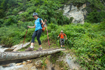 Woman walking across log with hiking poles in Nepal. 