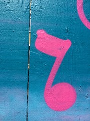 Hot pink painted music note on blue fence in Clarion Alley