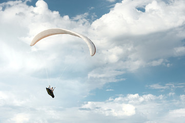 Professional paraglider flies on a white paraglider against the blue sky and white clouds....