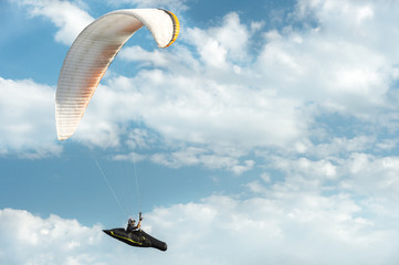 Professional paraglider flies on a white paraglider against the blue sky and white clouds....