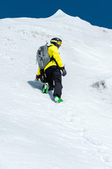 Fototapeta na wymiar A skier in a helmet and mask with a backpack rises on a slope against the background of snow and a glacier. Backcountry Freeride