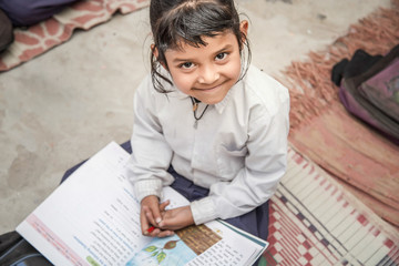 Adorable happy little preschooler girl, reading textbooks, school books. Wearing school uniform.