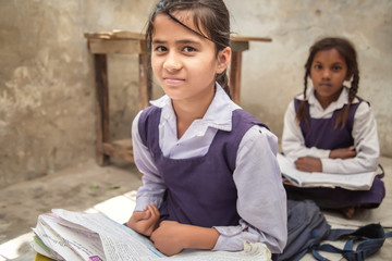 School girl in uniform of Indian Ethnicity sitting in their village classroom, looking at camera...