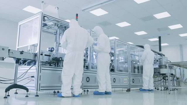 In the Manufacturing Facility Team of Scientist Wearing Sterile Protective Coverall Set's up / Programs Modern Industrial 3D Printer, High Precision Manufacture of Semiconductors under Process.