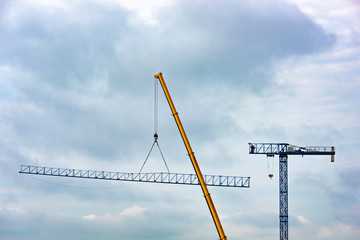 Setting up a blue tower crane in the construction site with a heavy mobile industrial yellow crane....