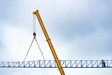 Setting up a blue tower crane in the construction site with a heavy mobile industrial yellow crane....