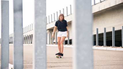 Young Beautiful Blonde Girl Riding Bright Skateboard on the Bridge