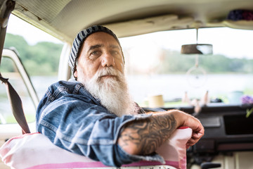Portrait of an old hipster sitting in a van looking at camera
