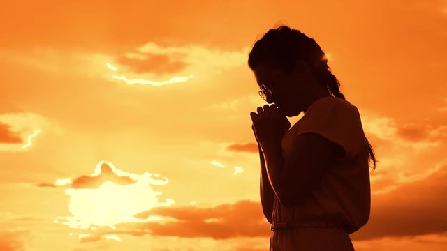 the girl prays. Girl folded her hands in prayer silhouette at sunset. slow motion video. Girl folded her hands in prayer pray to God. girl praying lifestyle asks forgiveness for sins of repentance