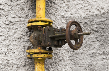 Old weathered gas crane and pipe on the background of a gray wall. Old gas gate of yellow colour is...
