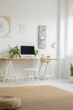 White chair at desk with computer desktop in home office interior with pouf on carpet. Real photo