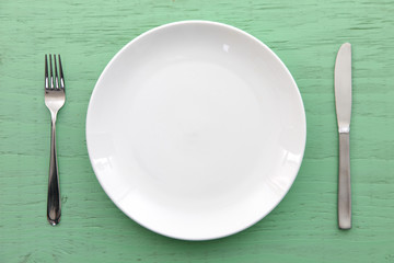 緑の木製テーブルに置かれた白い皿とカトラリー