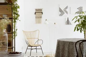 Real photo of a garden chair standing against white wall with macrame and monochromatic paintings...