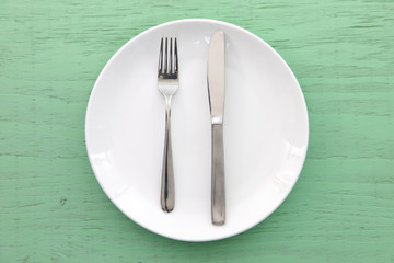 緑の木製テーブルに置かれた白い皿とカトラリーによる食事終了の合図