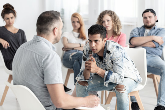 Rebellious spanish man listening to psychologist during group therapy for teenagers