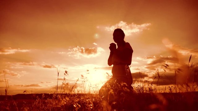 woman praying on her knees. Girl folded her hands in prayer silhouette at sunset. slow motion video lifestyle. Girl folded her hands in prayer pray to God. the girl praying asks forgiveness for sins