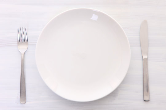 白い木製テーブルに置かれた白い皿とカトラリー