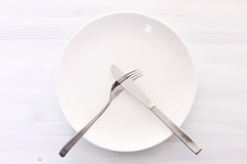 白い木製テーブルに置かれた白い皿とカトラリーによる不満足の合図