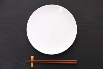 黒い木製テーブルに置かれた白い皿と箸