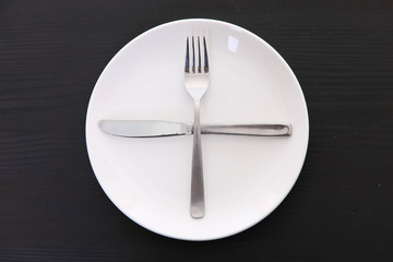 黒い木製テーブルに置かれた白い皿とカトラリーによる次の料理を待機の合図