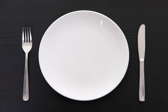 黒い木製テーブルに置かれた白い皿とカトラリー