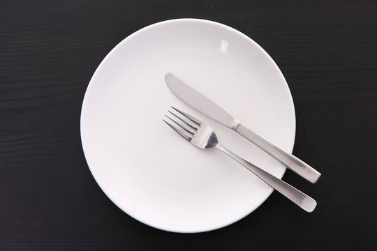 黒い木製テーブルに置かれた白い皿とカトラリーによる食事終了の合図