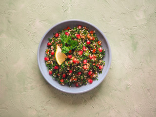 Salad with couscous and green herbs in a plate on the table.