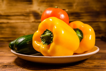 Ceramic plate with cucumbers, tomatoes and sweet pepper on wooden table