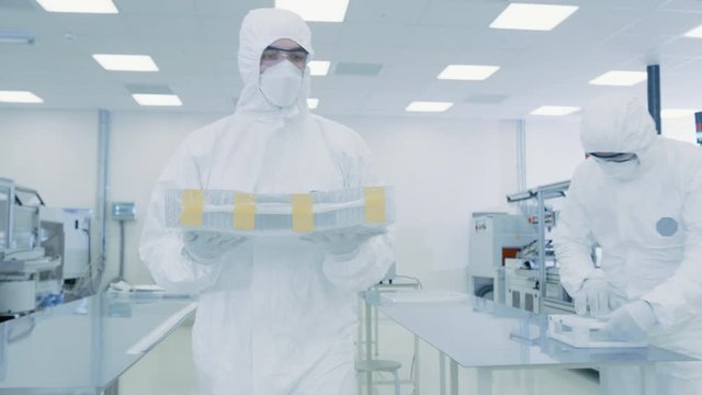 Scientist in Protective Suit Carries Case of Finished Product Through Laboratory