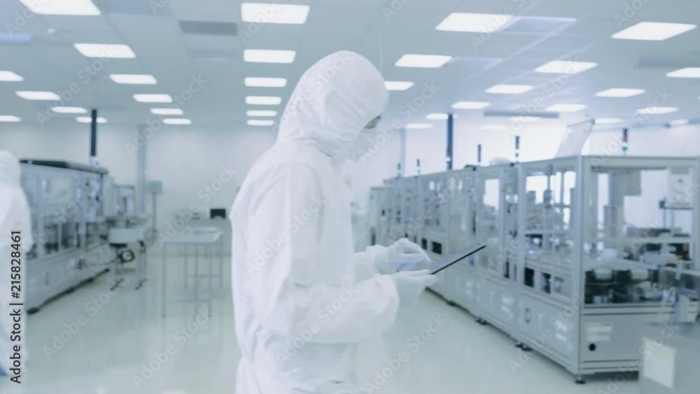 Poster scientist using digital tablet computer and wearing protective suit walks through manufacturing labo