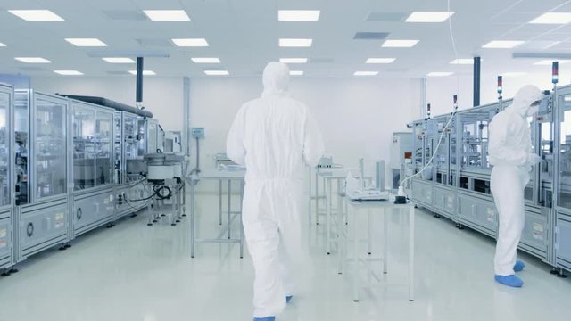 Scientist in Protective Suit Carries Case of Finished Product Through Laboratory. Workers in the Facility with Modern Industrial Machinery. 