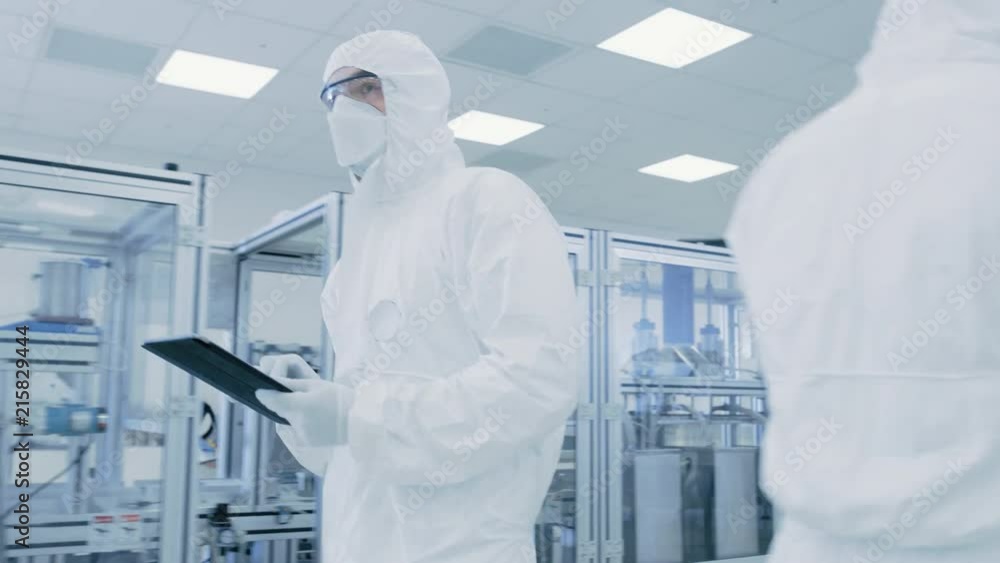 Poster quality control check: scientist using digital tablet computer and wearing protective suit walks thr