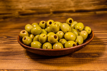 Ceramic plate with green olives on wooden table