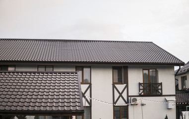 Modern roof covered with tile effect PVC coated brown metal roof sheets against cloudy sky.
