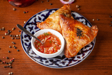Uzbek samsa in national plate with tomato sauce on a wooden table. end of the eastern baking.