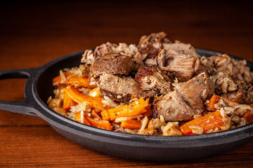 Traditional Uzbek oriental cuisine, pilaf or plov with large pieces of lamb meat and carrots, cooked in a black cast-iron skillet of kazan. Copy space, selective focus