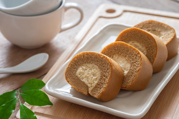 Coffee roll cake with cream on plate and coffee cup