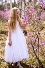 Fototapeta na wymiar A child stands among the ledum and birch in white dress, smiling and fly hair