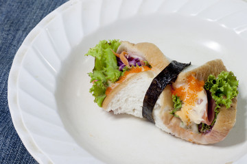 Junk food roll sandwiches with crab eggs, bacon, sliced with mayonnaise and seaweed on white plate put on the fabric.