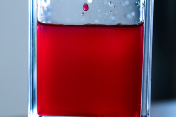Blood-red liquid in a transparent container illuminated from the back. Red color of a liquid