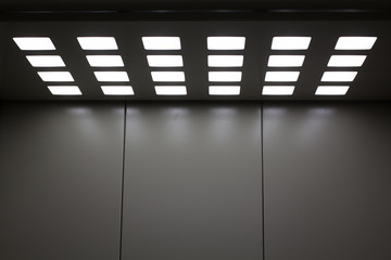 Gray metal elevator with square lamps in the ceiling