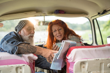 Old hipster couple sitting in a van and looking at a road map 