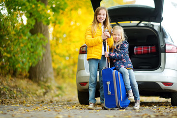 Two adorable girls with a suitcase going on vacations with their parents. Two kids looking forward...