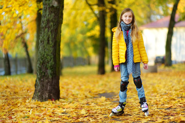 Pretty little girl learning to roller skate on beautiful autumn day in a park.