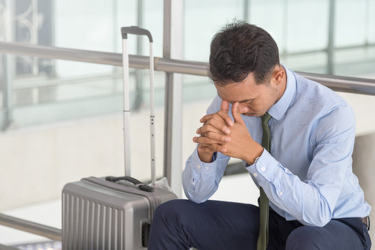 Serious businessman worrying something, sitting and touch his head at the airport terminal. Businessman miss his flight. Young man feeling sick before business trip.