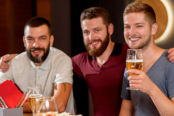 Three handsome men smiling, looking at camera and holding glass of beer.