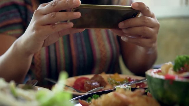 Attractive asian woman taking picture of a fruit salad on her smart phone at a table. Close up. Slow-motion
