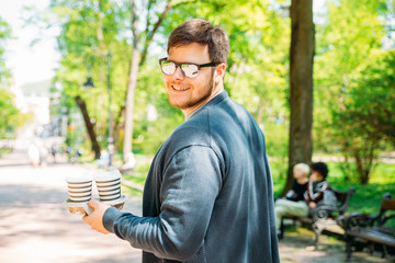 young adult walking with coffee by city park. lifestyle. summer day.