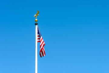The flag of the United States of America dangling at full-mast on a white pole topped with a golden...